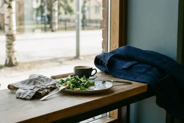 Kuvituskuva lounasravintolasta: salaatti, kahvikuppi ja ruokailuvälineet pöydällä.